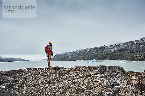 Chile  Torres del Paine Nationalpark  Lago Grey  Frau steht auf einem Felsen am Ufer und schaut auf einen Eisberg