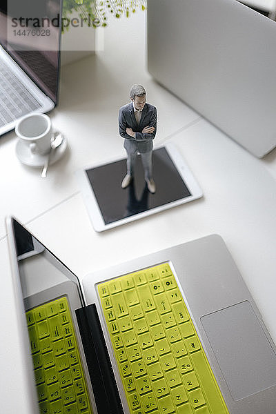 Geschäftsmann-Figur auf einem Schreibtisch stehend mit mobilen Geräten und einer Tasse Kaffee