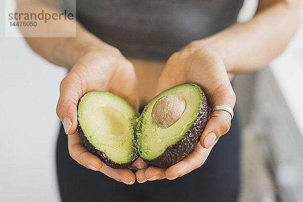 Hände einer Frau mit halbierter Avocado