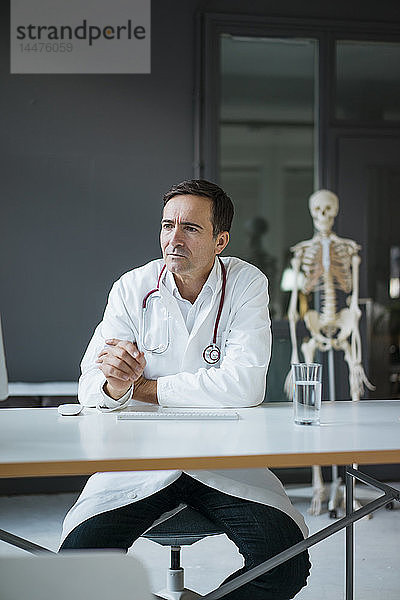 Am Schreibtisch sitzender Arzt in medizinischer Praxis mit Skelett im Hintergrund