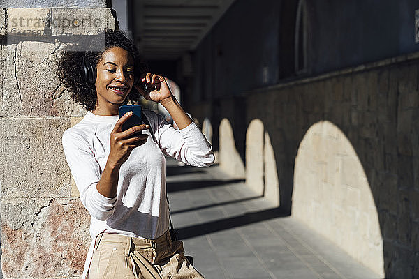 Junge lockere Geschäftsfrau mit Smartphone und Kopfhörern in der Stadt