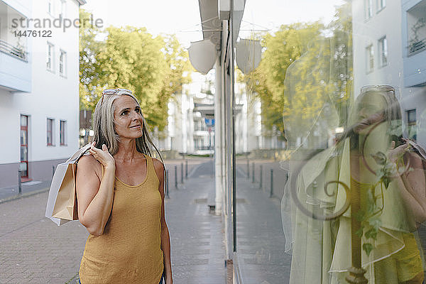 Porträt einer lächelnden Frau mit Einkaufstaschen  die in ein Schaufenster schaut