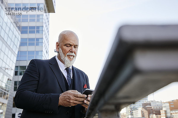 Eleganter Geschäftsmann mit Smartphone in der Stadt