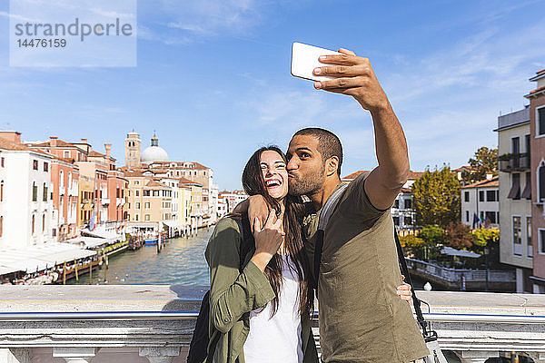 Italien  Venedig  glückliches junges Paar auf einer Brücke  das sich ein Selfie nimmt