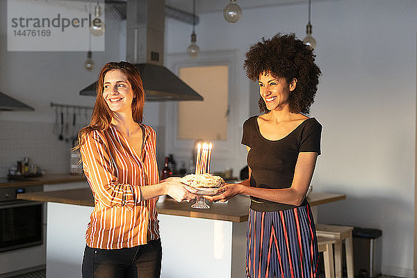Freunde bereiten einen Geburtstagskuchen mit brennenden Kerzen als Überraschung zu