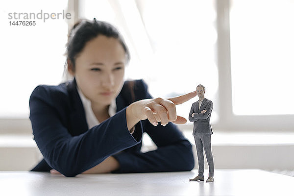 Geschäftsfrau beobachtet Geschäftsmann-Figur  stehend auf ihrem Schreibtisch