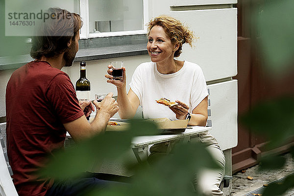 Glückliches Paar sitzt im Garten  isst Pizza  trinkt Wein