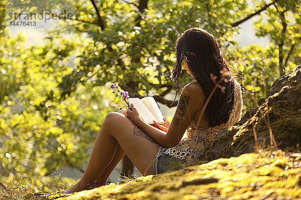 Junge Frau im Wald  die Blumen hält und ein Buch liest