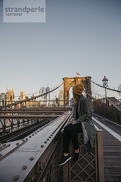 USA  New York  New York City  Touristin sitzt im Morgenlicht auf der Brooklyn Bridge