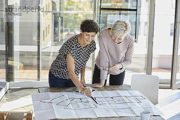 Zwei lächelnde Geschäftsfrauen diskutieren den Grundriss auf dem Schreibtisch im Büro