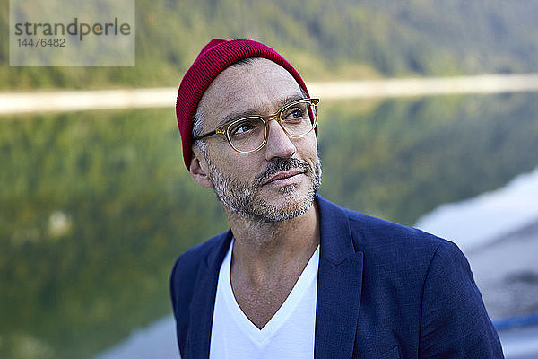Porträt eines bärtigen  reifen Mannes mit Brille und roter Mütze in Natur