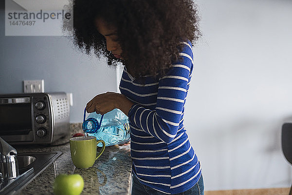 Junge Frau gießt Wasser in einen Becher in ihrer Küche