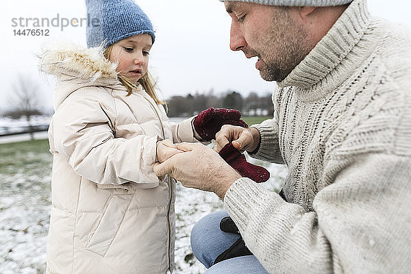 Vater hilft Tochter beim Anziehen von Handschuhen im Winter