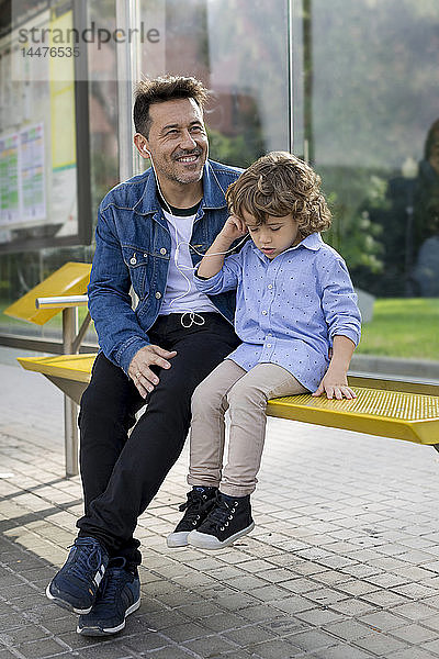 Vater und Sohn sitzen an der Straßenbahnhaltestelle in der Stadt und teilen sich Ohrstöpsel