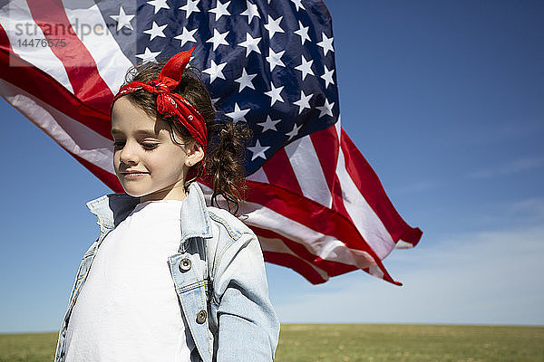 Mädchen mit amerikanischer Flagge auf Feld in entlegener Landschaft