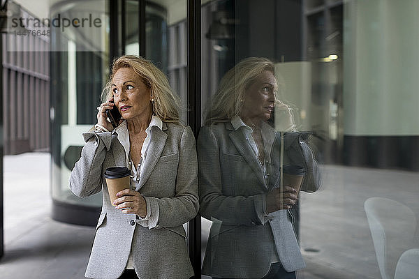 An die Glasfront gelehnte ältere Geschäftsfrau telefoniert mit dem Handy