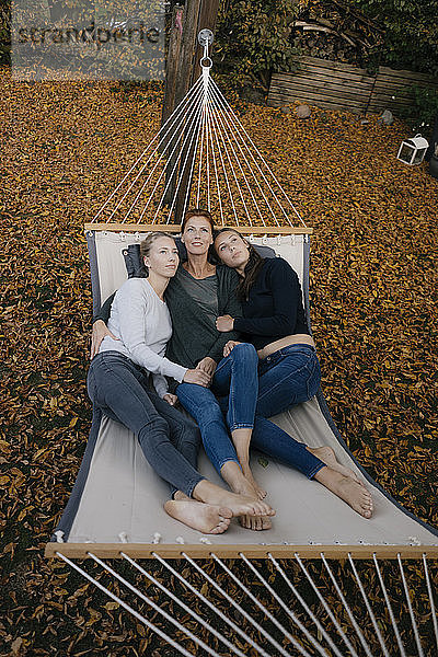 Mutter mit zwei jugendlichen Mädchen  die im Herbst in der Hängematte im Garten liegen