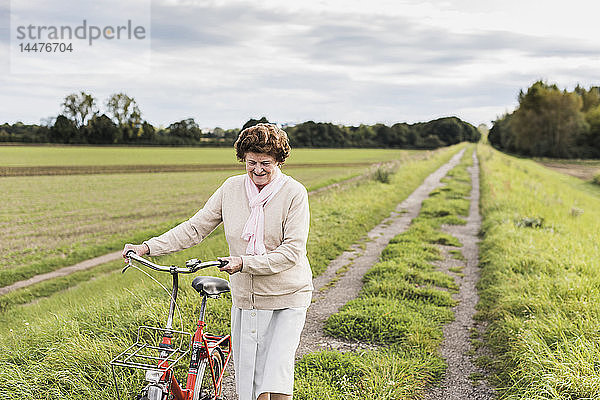 Ältere Frau schiebt Fahrrad in ländlicher Landschaft