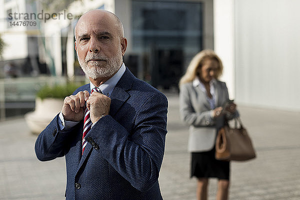 Leitender Geschäftsmann passt seine Krawatte an Geschäftsfrau im Hintergrund an