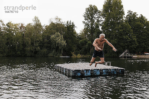 Älterer Mann springt in einem See vom Floß