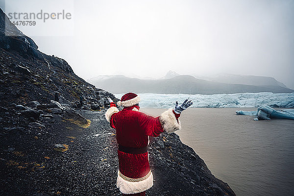 Island  Rückenansicht des vor dem Gletscher stehenden Weihnachtsmanns