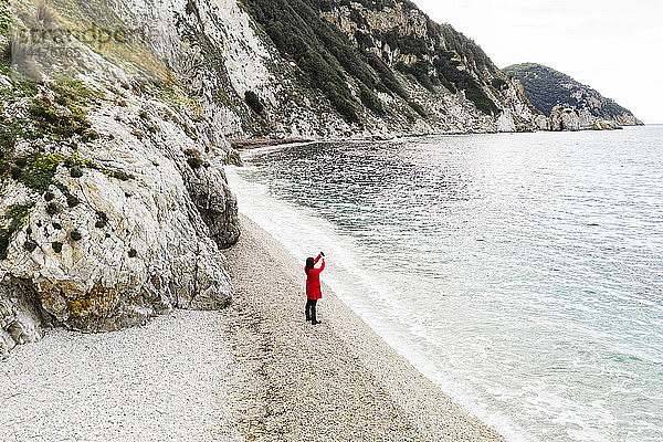 Italien  Elba  Frau mit rotem Mantel beim Fotografieren am Strand  Luftaufnahme mit Drohne