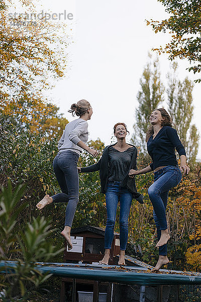 Glückliche Mutter mit zwei Mädchen im Teenageralter  die im Herbst im Garten auf dem Trampolin springen