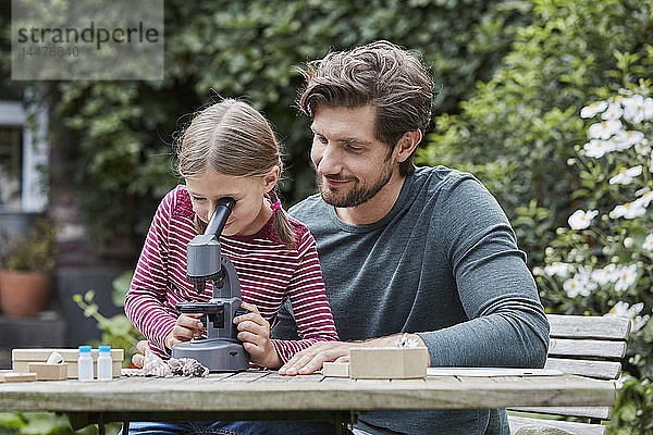 Vater und Tochter benutzen gemeinsam das Mikroskop am Gartentisch