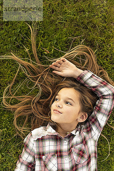 Bildnis eines lächelnden Mädchens mit langen Haaren auf einer Wiese liegend