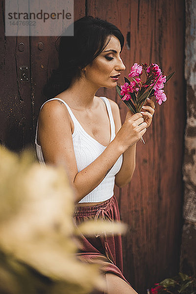 Frau lehnt an Holztür und riecht nach rosa Blumen