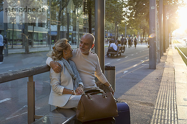 Spanien  Barcelona  älteres Ehepaar mit Gepäck sitzt bei Sonnenuntergang an der Straßenbahnhaltestelle in der Stadt