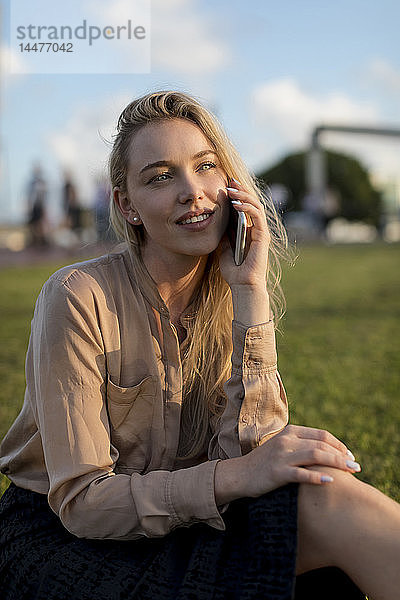 Lächelnde junge Geschäftsfrau am Handy auf einer Wiese