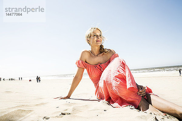 Frau im Kleid am Strand sitzend