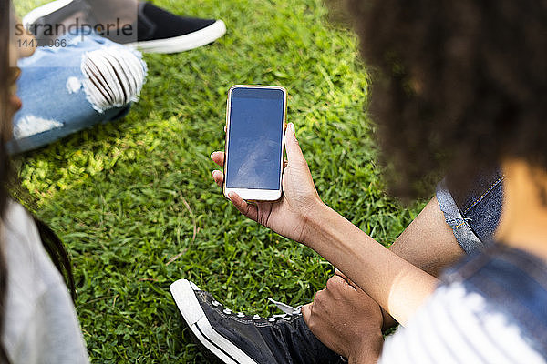 Junge Frau verbringt mit Freunden Zeit in einem Park und hält ein Smartphone in der Hand