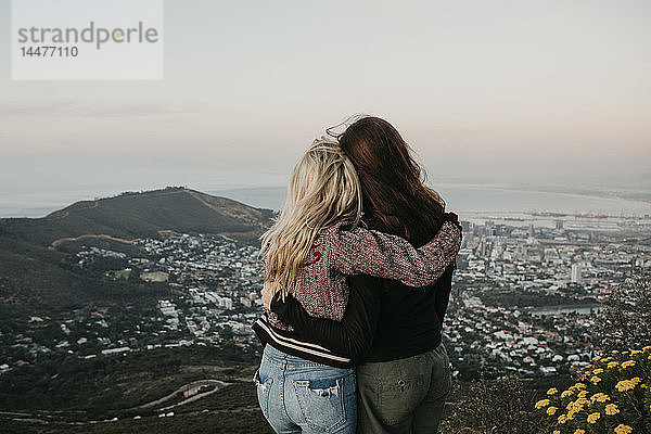 Südafrika  Kapstadt  Kloof Nek  Rückansicht von zwei Frauen  die sich bei Sonnenuntergang umarmen