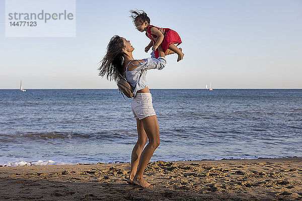 Mutter und Tochter amüsieren sich am Strand und tun so  als würden sie fliegen