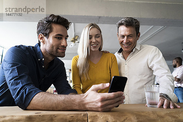 Lächelndes Geschäftsteam beim gemeinsamen Betrachten des Mobiltelefons im Loft-Büro