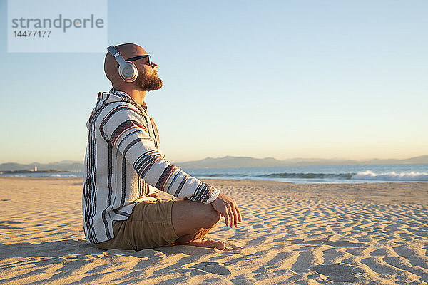 Mann mit Kopfhörern am Strand sitzend