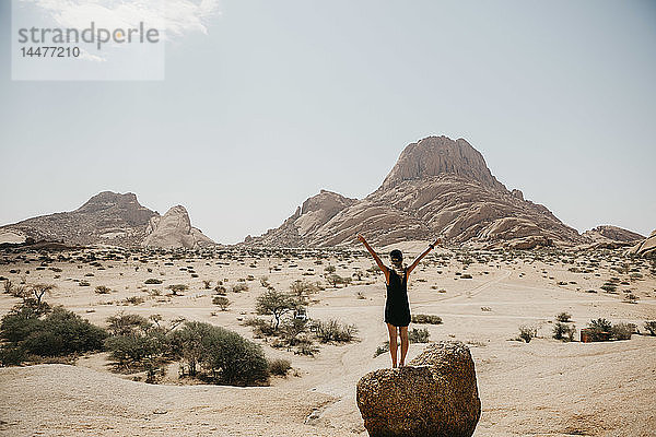 Namibia  Spitzkoppe  Rückansicht einer auf einem Felsen stehenden Frau mit erhobenen Armen