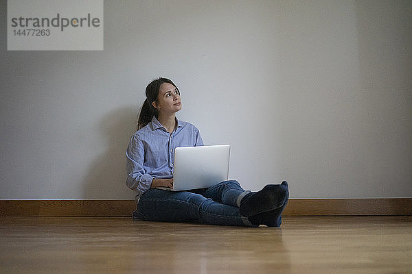 Junge Frau sitzt auf dem Boden und benutzt einen Laptop