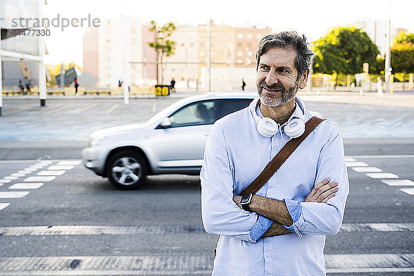Porträt eines lächelnden reifen Mannes mit Kopfhörern  der an einer Straße steht