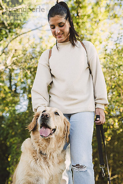 Lächelnde junge Frau mit ihrem Golden-Retriever-Hund in einem Park