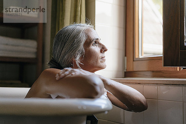 Porträt einer nachdenklichen Frau in der Badewanne  die aus dem Fenster schaut