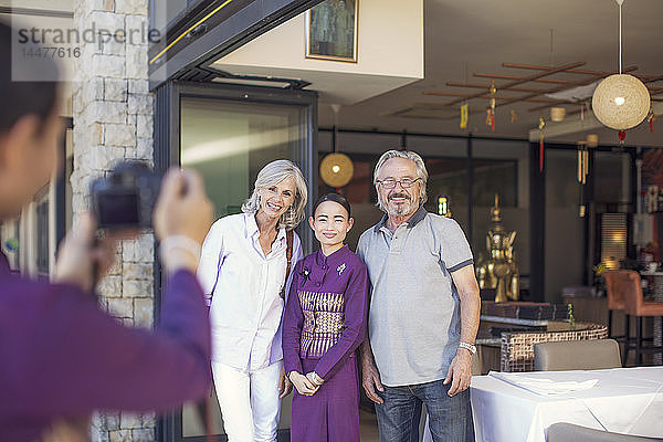 Älteres Ehepaar beim Fotografieren mit asiatischer Kellnerin vor einem Restaurant