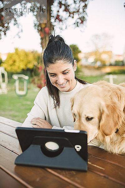 Lächelnde junge Frau mit einer Tablette in einem Park mit ihrem Hund