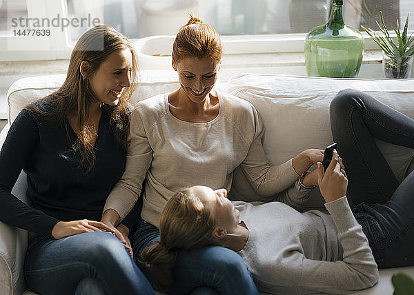 Glückliche Mutter mit zwei Teenager-Mädchen auf der Couch zu Hause mit Handy