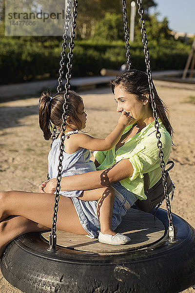 Glückliche Mutter mit Tochter auf Reifenschaukel auf einem Spielplatz