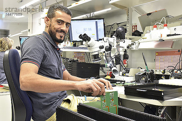 Porträt eines lächelnden Mannes  der an der Qualitätskontrolle bei der Herstellung von Leiterplatten für die Elektronikindustrie arbeitet