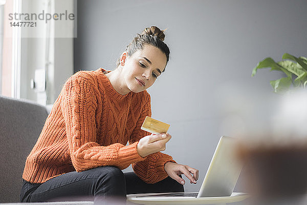 Porträt einer zufriedenen Frau  die mit Laptop und Kreditkarte auf der Couch sitzt