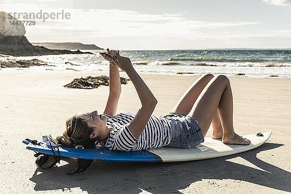 Junge Frau am Strand  auf dem Surfbrett entspannen  Smartphone benutzen